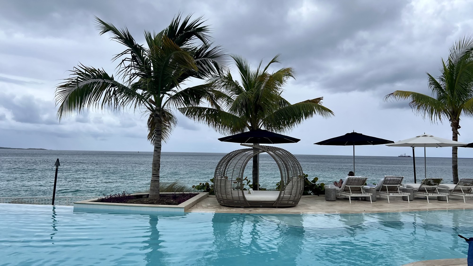 Infinity pool with woven cabana and palm trees overlooking the ocean