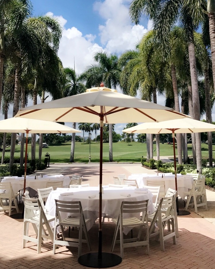 Poolside event dining under cream umbrellas, palm-lined lawn