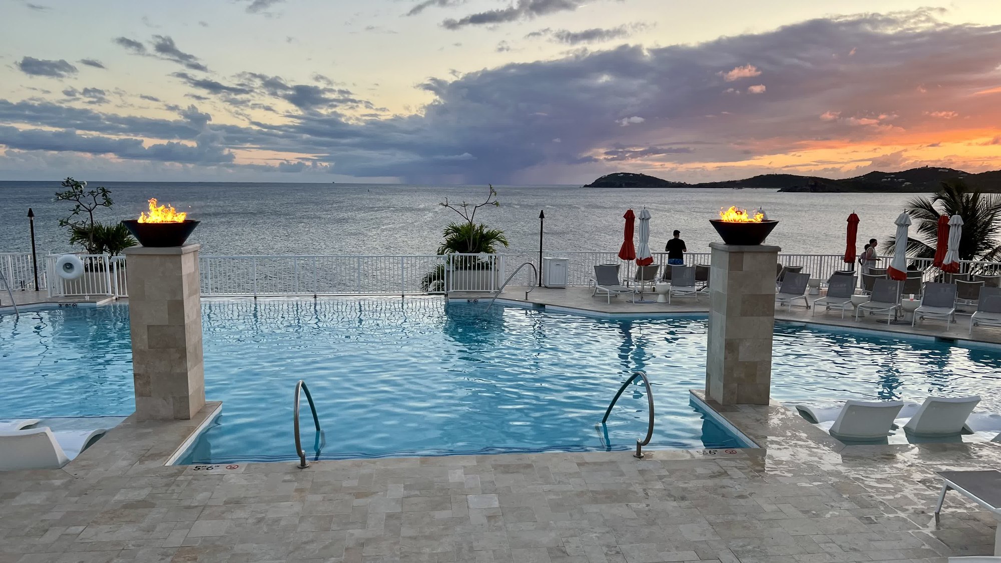 Infinity pool at sunset with lit firebowls